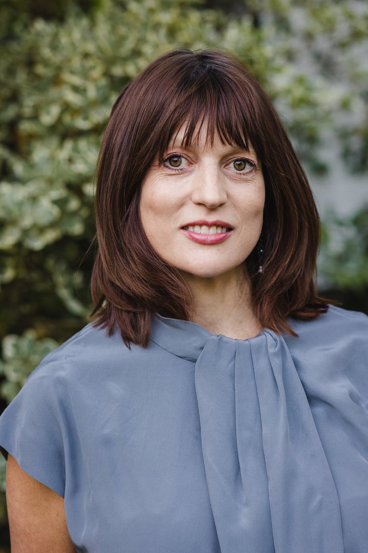 Portrait of a woman with shoulder length brown hair wearing a light blue shirt smiling and looking directly into the camera. 