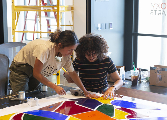 Photo of two students working on a colorful artwork installation. Both are looking down and focusing on their work. 