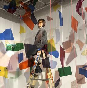 Debra Scacco on a ladder in a colorful installation of rainbow pieces of glass