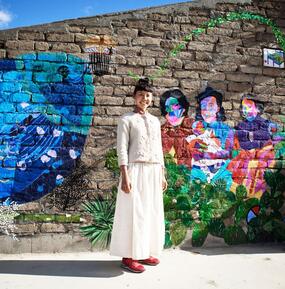 Artist iris yirei hu standing in front of a brick wall with several murals. 