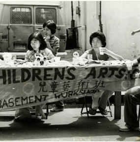 Table set up outdoors with a banner and several people sitting around the table.