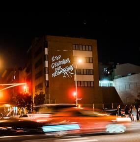 Nighttime city image with "stop gentrifying our neighborhoods" written on a building.