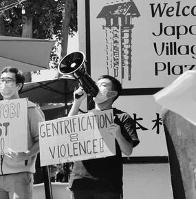 Black and white photograph of a group of people holding protest signs in Little Tokyo, Los Angeles, CA