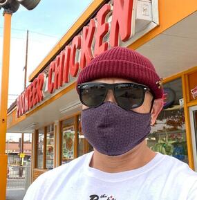Johneric Concordia wearing a beanie, sunglasses and a mask in front of the Pioneer Chicken restaurant.