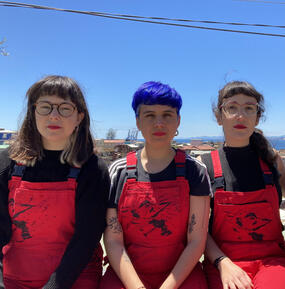Three people (LASTESIS) wearing matching red overalls look at camera