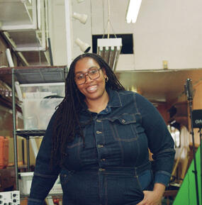 medium portrait of artist, smiling, wearing blue button-up shirt and glasses