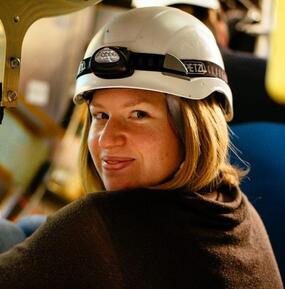 over the shoulder close up of the artist looking directly to camera, wearing a white hard hat and a headlamp