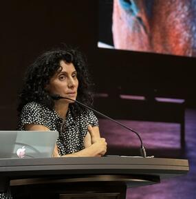 medium shot, full color, of Oraib Toukan leaning on a lectern