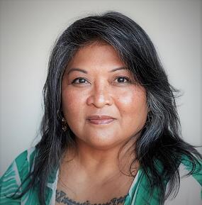 Portrait of a woman with dark hair wearing a green shirt looking directly into the camera. She has a light smile. 