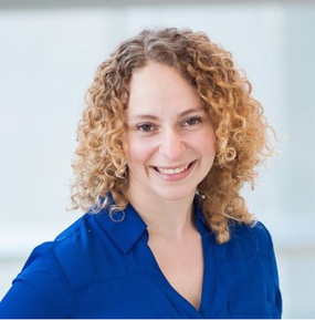 A smiling woman in a royal blue shirt with blonde curly hair. 