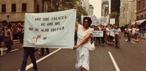 Archival image of Sylvia Rivera walking in a protest holding a large banner 