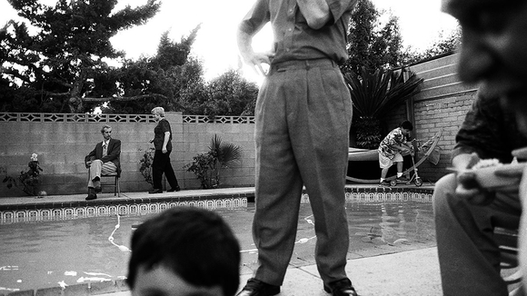 black & white photo of people standing around a pool, foreground & background