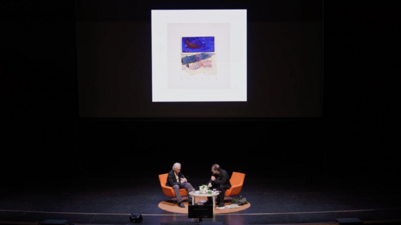 wide shot of Ed Ruscha and Paul Holdengräber on stage, with a projected image behind