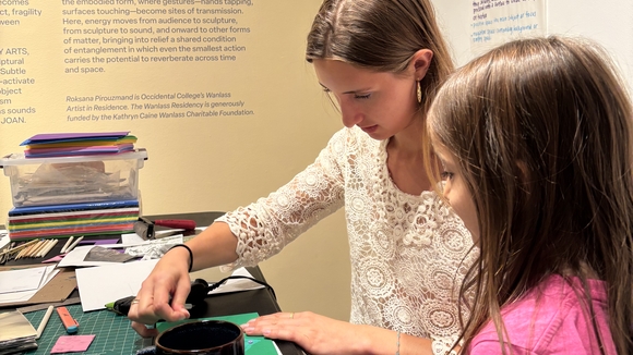Two people are creating an art project together in a gallery space. One is older and one is younger. 