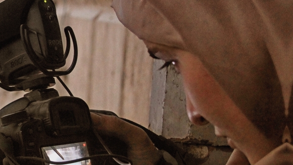 The cover of Refugee Cinema by Bruce Bennett and Katarzyna Marciniak shows a close-up of a woman in a headscarf looking down at a Canon camera's flip screen while filming, set against a weathered plaster wall.