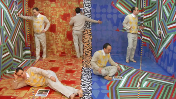 Five versions of the same man stand, sit, and lie down around a psychedelic room