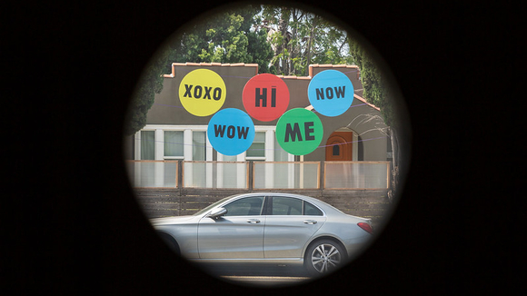 Lens with a view of the sidewalk and circular multi color signs with different sayings: "xoxo" "hi" "now" "wow" "me"