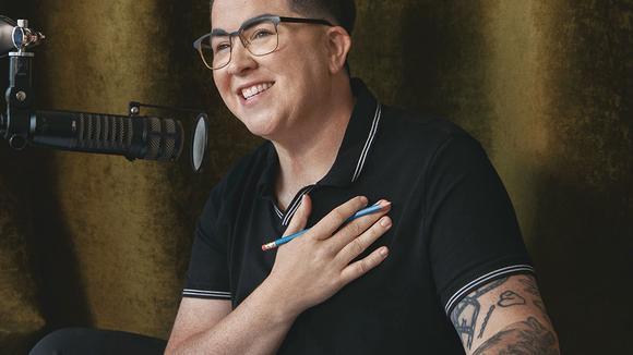 medium of V Spehar smiling with hand to chest and podcast microphone camera left