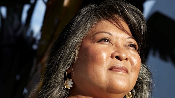 Portrait of a woman with long hair looking into the distance. She is wearing a green top. 