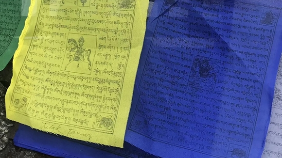 Close up photo of prayer flags, one yellow one blue. 