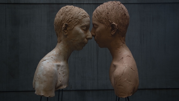 color image of two sculptural busts in profile, with faces touching