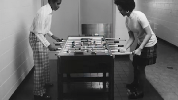 Black and white photograph of two Black people playing foosball 