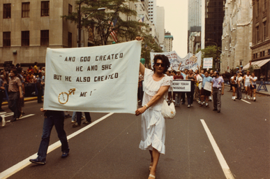 Archival image of Sylvia Rivera walking in a protest holding a large banner 
