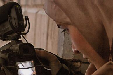 The cover of Refugee Cinema by Bruce Bennett and Katarzyna Marciniak shows a close-up of a woman in a headscarf looking down at a Canon camera's flip screen while filming, set against a weathered plaster wall.
