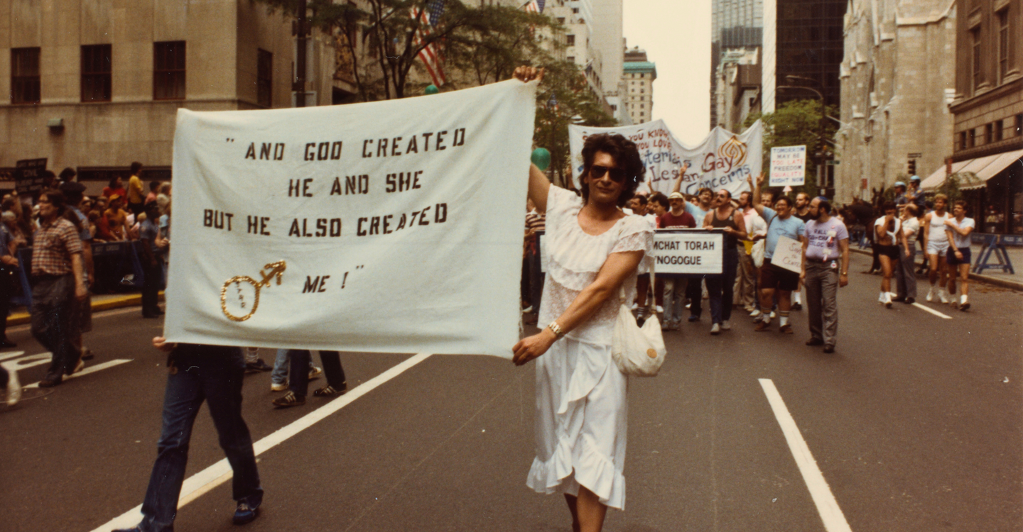 Archival image of Sylvia Rivera walking in a protest holding a large banner 