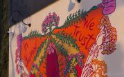A colorful painted mural of a yonnic flower that reads "in yarrow we trust"