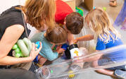 Several children and one adult putting objects into tubes that are connected to an air vent. 
