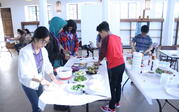 students standing around folding table and making food 