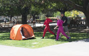 two performers in red and pink bringing a passerby into an orange camping tent