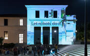 projection on building of tropical island with the words "let robots do it'