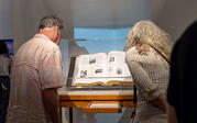 Two people leaning in to read a large book, "The Encyclopedia of Invisibility," in a glass vitrine.