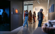 People looking at artwork, with a standing person in the center using headphones and looking at a photograph of a black hole.