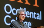 Professor Mary Beth Heffernan introducing Travares Strachan at a podium, with OXY logo projected behind.