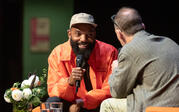 Tavares Strachan sitting and laughing as he speaks into a microphone to Paul Holdengräber.