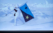 Far view of Tavares Strachan and Paul Holdengräber on stage, with an audience below and Strachan's artwork projected above: him walking through the snow with a flag.