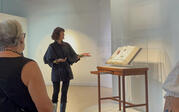 Yael Lipschutz explaining the Encyclopedia of Invisibility at the center of the gallery surrounded by a group of people.