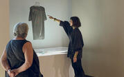 Curator Yael Lipschutz discussing and pointing to the Cosmic Bitcasting dress artwork, with a person onlooking.