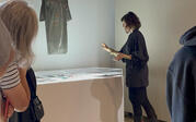 Curator Yael Lipschutz discussing the Cosmic Bitcasting dress artwork, with a group onlooking.