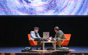 over audience wide of Kip Thorne and Paul Holdengraber on stage, with Lia Halloran painting projected behind