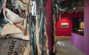 Entry to exhibition immersed in floor-to-ceiling installation collage by Alicia Piller using scrap paper and branches. Farther is the entry to the next room of exhibition. 