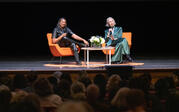 Full view of Robin Coste Lewis and Alexandra Grant sitting on stage. Lewis laughs while Grant tells a story, looking to the right.