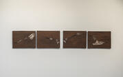 Straight-on view of the right 4 panels of Roksana's diptic piece "from one room to another." Dark wooden panels are carved with lineart that depicts two bodies curled in fetal position on the ground, their backs forming rolling curves and their feet a lighter painted color.