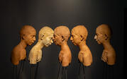 Frontal view of Roksana's ceramic work "Land." Five casted unglazed clay busts of the artist levitate at eye level in profile, mounted on steel rods.