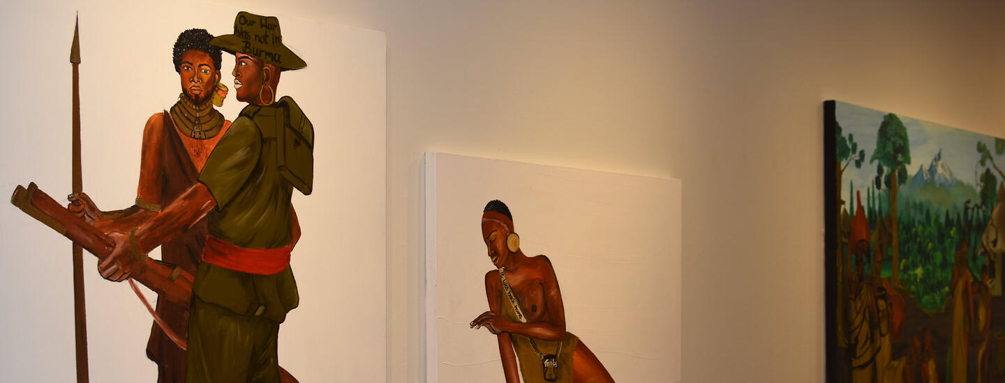 Three paintings of African people hang on a white wall