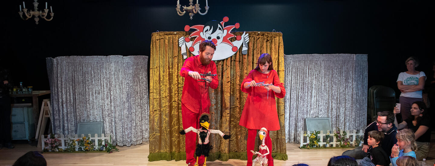 Two puppeteers with bird puppets perform as an enraptured audience watches