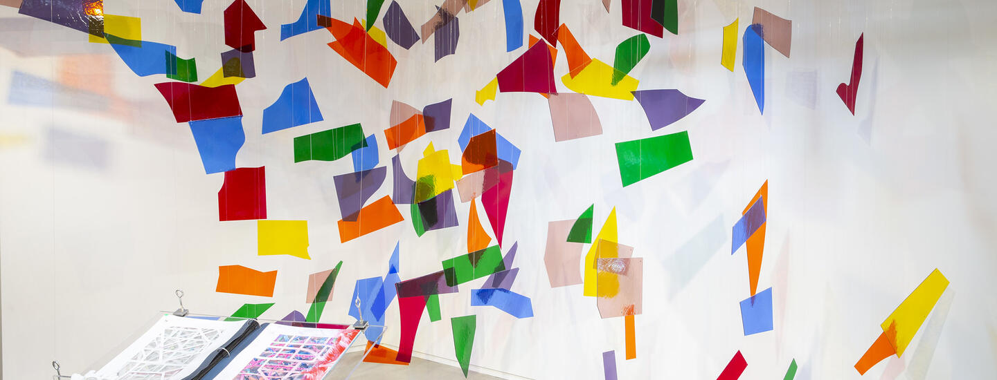 Multicolored transparent shards are suspended from the ceiling in the background, with a book hanging in the foreground